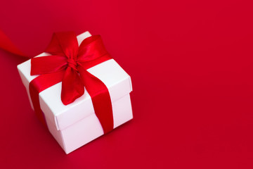 White box with a red ribbon on a red background, copy space. Greeting card concept