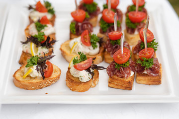 Close-up big plate with serving snack canapes fried bread tomato parsley and salami. Appetizing fresh unhealthy sandwich food decorated on table of luxury restaurant