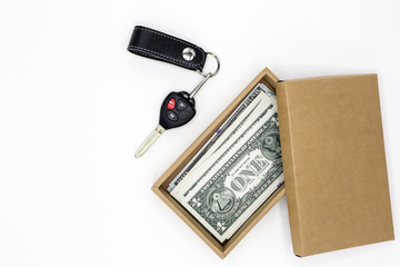 Car key and banknotes in a small gift cardboard box on white background.