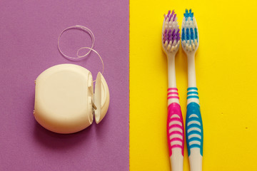 Two toothbrushes and dental floss . Yellow and violet background