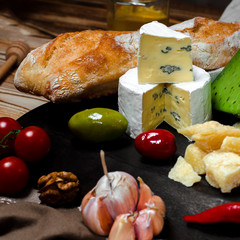 Mix cheese on dark background on wood board with grapes, honey, nuts, tomatoes and basil. Top view.