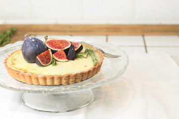 gorgeous round french classic homemade shortcake pastry dough vanilla custard tart cake decorated with figs and rosemary on glass stand near with retro fork on grey table cloth. Insta food photo style