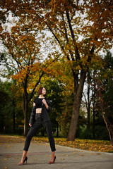 A tall leggy young beautiful and elegant model woman at formal wear posed at autumn background.