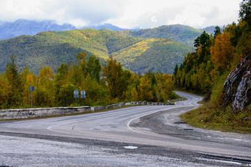 A curving autumn road with colorful forest and mountain in the far distance