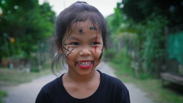 Asian little girl with a painted face is posing facial expression and walking alone in halloween. The children in demon costumes to celebrating halloween. Kids trick or treat. Slow motion.