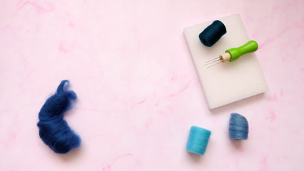 Flat lay of blue felt wool rolls and felting kit of felt needle and sponge.