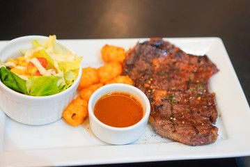 Grilled beef steaks served with fresh salad, hash browns potato and spicy sauce on white dish....