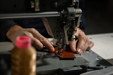 Working process of leather craftsman. Tanner or skinner sews leather on a special sewing machine, close up.