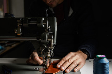 Working process of leather craftsman. Tanner or skinner sews leather on a special sewing machine, close up.
