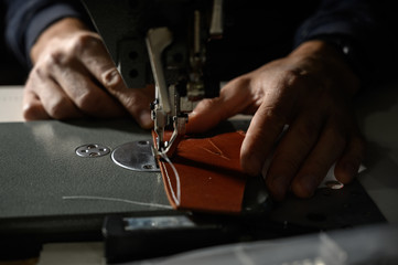 Working process of leather craftsman. Tanner or skinner sews leather on a special sewing machine, close up.