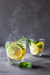 Cold refreshing drink with lemon, mint and ice in a glass on a gray wooden background.