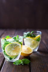 Cold refreshing drink with lemon, mint and ice in glasses on a dark wooden background.