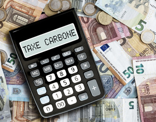 close-up of text TAXE CARBONE, French for carbon tax, on display of pocket calculator against euro bills on table
