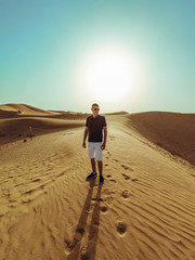 Young beautiful man walks along the sand dunes of the Dubai desert