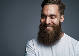 Smiling bearded hipster standing against a gray background