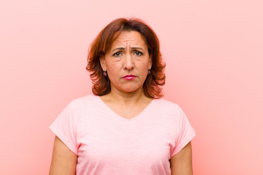 middle age woman feeling sad and whiney with an unhappy look, crying with a negative and frustrated attitude against pink wall