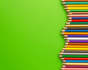 Colored pencils next to each other top view. Marketing and development theme. Crayons on green background with copy space. Back to school.