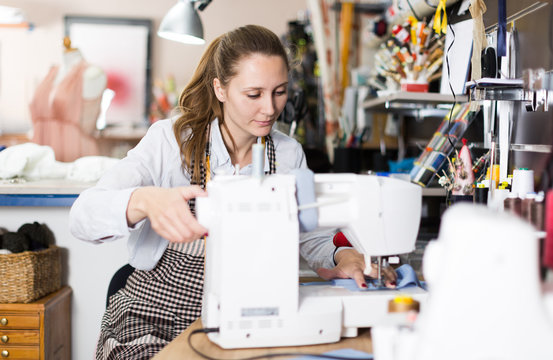 Female seamstress is sitting near sewing machine and create new dress