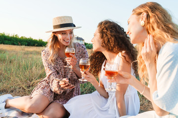 Photo of delighted young women using cellphone while drinking red wine