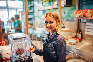 Portrait of a cheerful waitress preparing fresh juice.