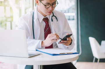 An Asian doctor is using a smartphone on a white desk at a hospital. Intelligent Health Technology Concepts