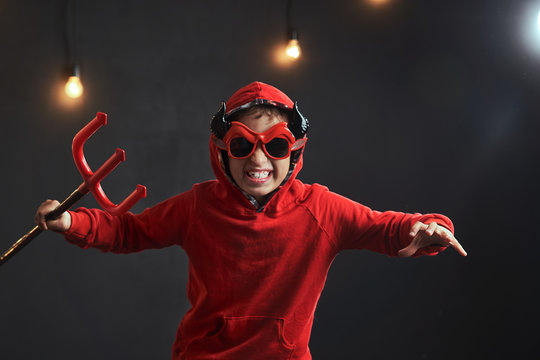 child in a red hoodie wearing a hood on his head with a red pitchfork in his hands in the image of the devil scares on Halloween