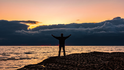 Traveler man on a rocky seashore at dramatic sunrise time