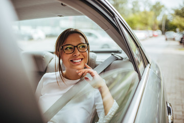 Portrait of a happy young woman in back seat of car looking out of window.