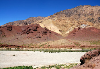 The Hari River (Harirud) near Chisht-e-Sharif in Herat Province, Afghanistan. A view of the river bank with colorful mountain scenery in a remote part of western Afghanistan. Red and orange colors.