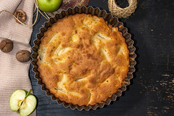 Apple Pie Charlotte on a black wooden table with green apples in iron form.