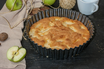 Apple Pie Charlotte on a black wooden table with green apples in iron form.