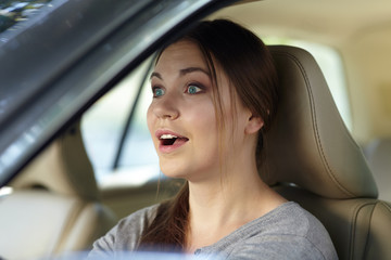 Young attractive caucasian woman behind the wheel driving a car with grimace of astonishment or shock, mouth opened. Strong emotions, wow expression. Copy space.