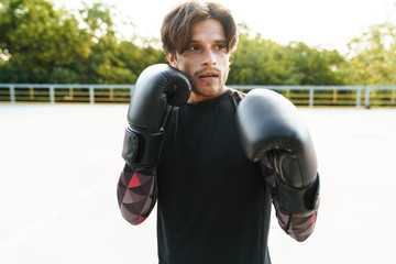 Photo of young focused man doing workout in boxing gloves