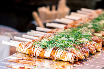 Okonomiyaki on wooden sticks with soy sauce and mayonaise topped with green onion at Nishiki...