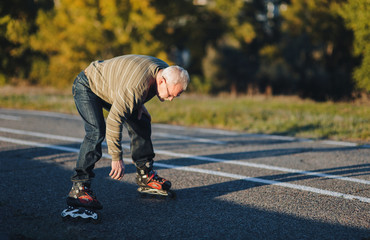 Fototapeta premium The old man on the rollers is tired and resting. Active retiree. Sports activities in old age. Copy space. Pensioner.