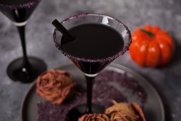 Two glasses with black cocktail, dried roses for Halloween party on the dark background