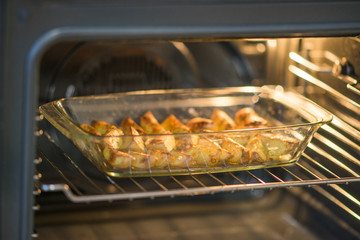 ready baked potato slices with spices lie in glass dish in the oven.