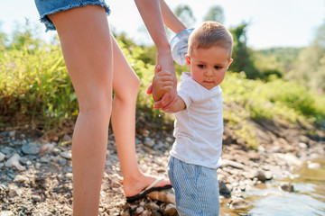 Young woman mother hold her little small boy son while walking by the river or lake water in sunny day