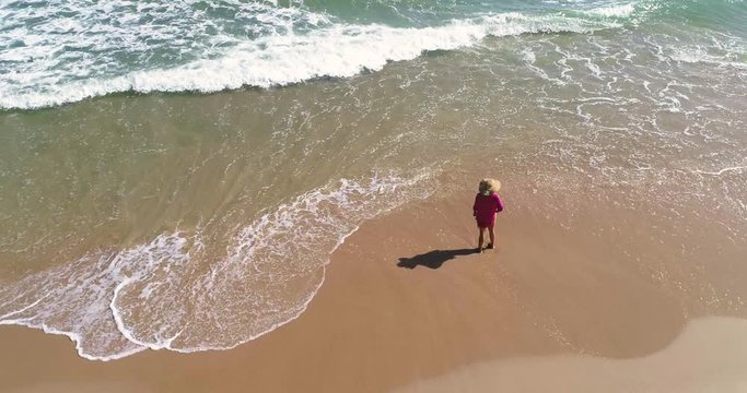 Mujer mirando el horizonte en playa de arena dorada y mar turquesa con dron volando