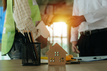 Contractor. wooden house model on workplace desk with construction worker team handshake greeting start up plan new project contract in office center at construction site and partnership concept