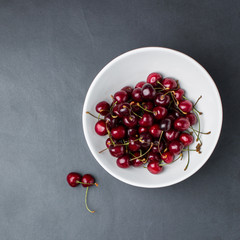 Fresh cherries in a white plate on a concrete, marble table / background