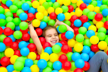 Funny child girl having fun in ball pit with colorful balls.