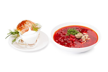 A plate of real Ukrainian borscht with meat. Separately, there is a saucer with sour cream and a garlic pampushka. Isolated on a white background.