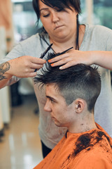 Obraz na płótnie Canvas Hairdresser haircutting styling young man's hair in barbershop. Young woman working as a hairdresser in hair salon. Real people, authentic situations