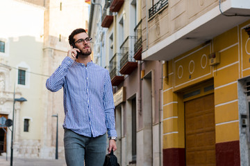 Young businessman is walking on the street while he is talking with his phone