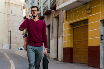 Young businessman is walking on the street while he is talking with his phone