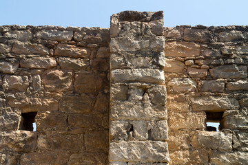 Close-up of an old ruined stone wall with two small holes and the clear blue sky above 