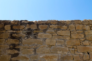 Old stone brick wall with blue sky above 