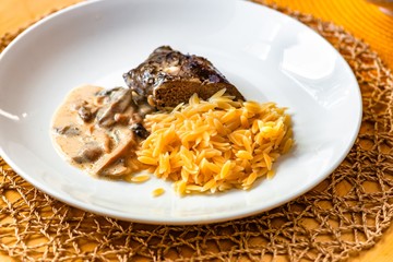 Boiled pasta rice (orzo),mushroom sauce, deeer on plate.