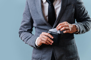 Businessman in a suit pulling credit card from his wallet over blue background - obrazy, fototapety, plakaty